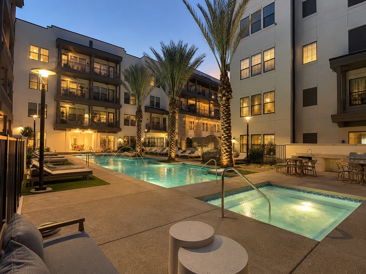 Pool courtyard at dusk with palm trees and lit balconies